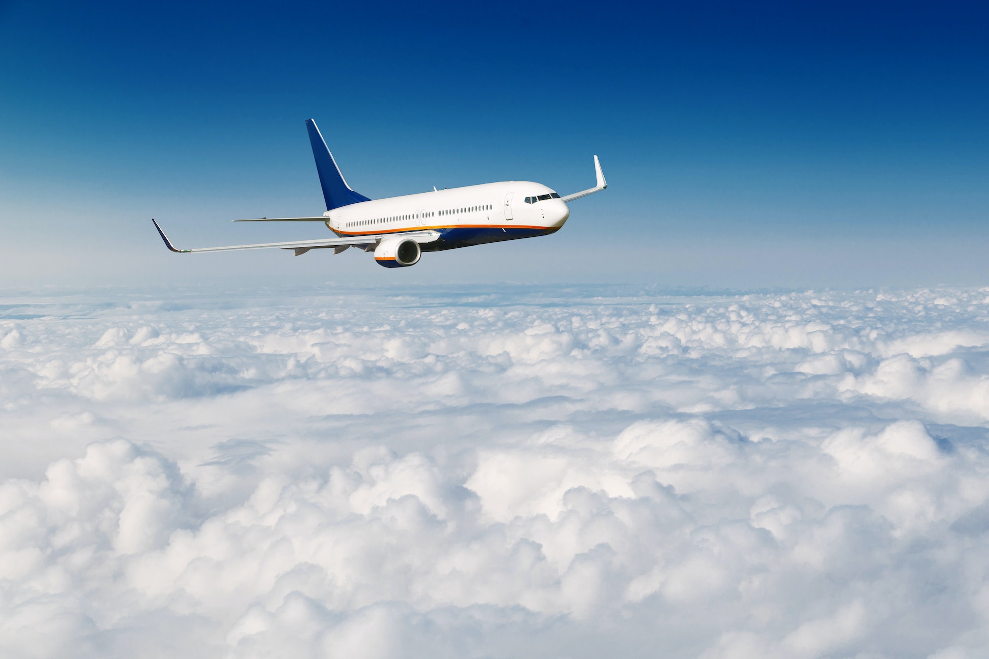 Commercial airplane flying above clouds on blue sky background.