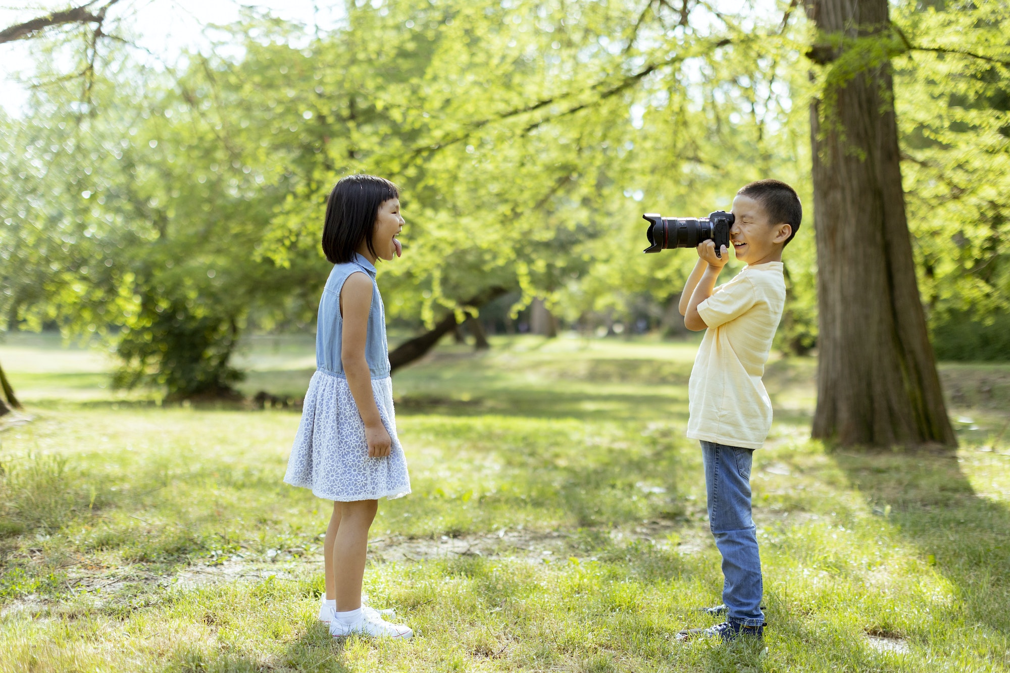 Little asian boy acting like a professional photographer while taking photos of his little sister