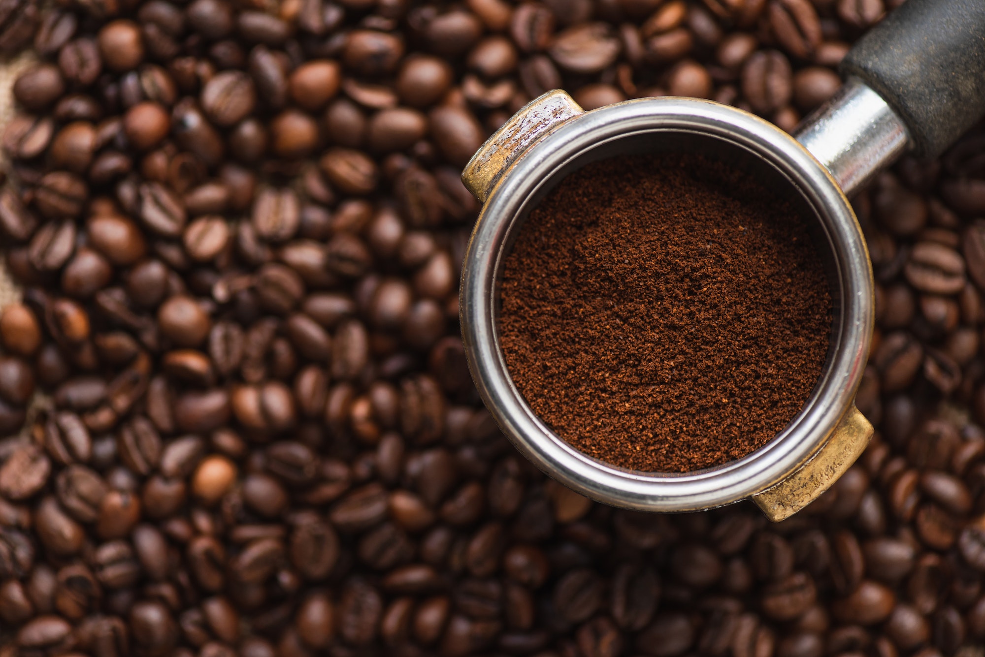 top view of ground coffee in portafilter on coffee beans background